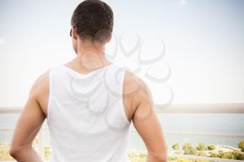 Young adult Caucasian man in white shirt starring at the sea in bright summer day, rear view
