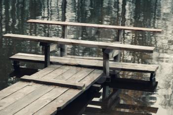 Wooden bench on the end of floating pier, still lake coast. Vintage toned photo, old style filter effect