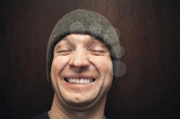 Young laughing man in gray hat. Closeup face portrait over dark wooden wall background, selective focus
