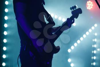 Live rock music background, electric bass guitar player in blue stage lights, closeup photo with soft selective focus