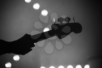 Live music background, electric bass guitar over blurred stage lights, close-up black and white silhouette photo with soft selective focus