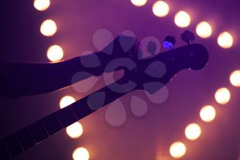 Live music background, guitarist tunes electric bass guitar, close-up photo with soft selective focus and colorful illumination
