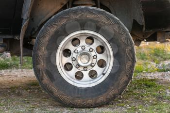 Closeup photo of SUV car wheel on dirty rural road with grass, front view