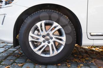 Closeup photo of white modern car wheel on cobble road with fallen autumnal leaves