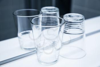 Two empty glasses stand on white shelf near the mirror, blue toned closeup photo