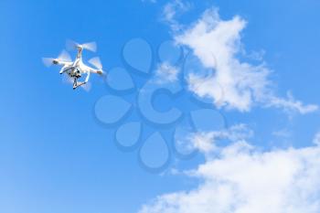 Quadrocopter in cloudy sky, compact white drone controlled by wireless remote