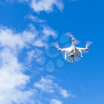 White quadrocopter in cloudy sky, compact drone controlled by wireless remote