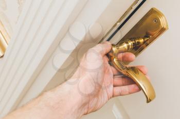 Male hand opens white wooden door with golden handle, closeup photo with selective focus