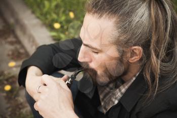 Young asian bearded man smoking pipe in summer park, close up portrait