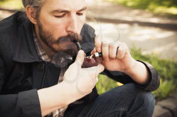 Young asian bearded man smoking a pipe in summer park, close-up portrait with selective focus