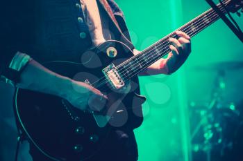 Electric guitar player on a stage in green lights, soft selective focus