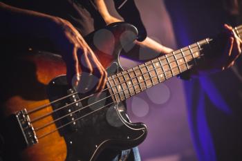 Close-up photo of bass guitar player hands, soft selective focus, live rock music theme