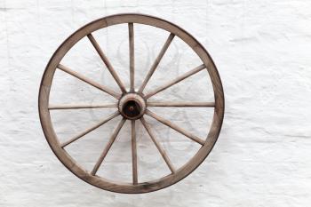 Old wooden cart wheel hanging on white rural wall