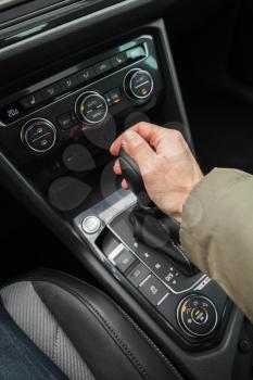 Driver hand holds gear lever of modern luxury car. Close up photo with selective focus
