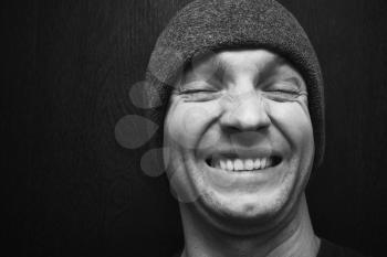 Young laughing man in gray hat. Closeup face portrait over dark wooden wall background, selective focus, black and white photo