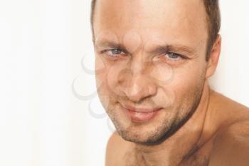 Close up face portrait of young adult shirtless smiling man over white wall background