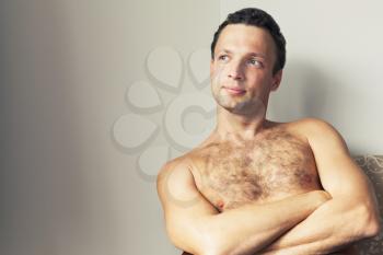 Portrait of young European shirtless man sitting near white wall