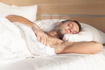 Portrait young European man sleeping in bed on white linen in morning light