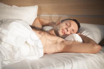 Portrait young European man sleeping in bed on white linen in morning sunlight