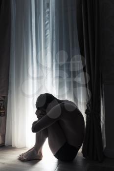 Young sad man sitting in dark room near the balcony door at night