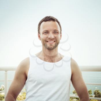 Outdoor summer portrait of Young sporty smiling European man in white shirt, vintage toned square photo