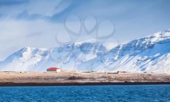 Coastal Icelandic landscape with snowy mountains and living house under dramatic blue sky. Reykjavik area, Iceland