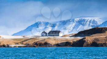 Coastal Icelandic landscape with snowy mountains and white living house under dramatic blue sky. Reykjavik area, Iceland
