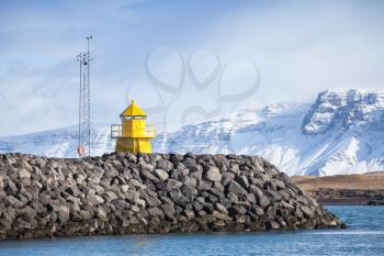 Yellow lighthouse tower on stone breakwater, entrance to Reykjavik industrial port