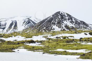 Misty Icelandic landscape with snow, green moss growing on rocks and rocky mountains, South coast of Iceland