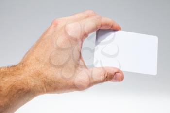 Male hand with white empty card over gray background, close up photo, selective focus