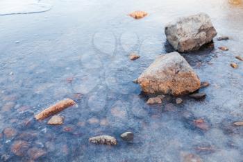 Stones lay on Saimaa lake coast covered with ice