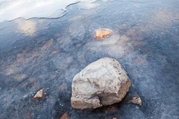 Stone lays on Saimaa lake coast covered with ice