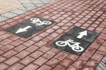 Bicycle lane, road marking with arrows and bike icons over brown cobble road
