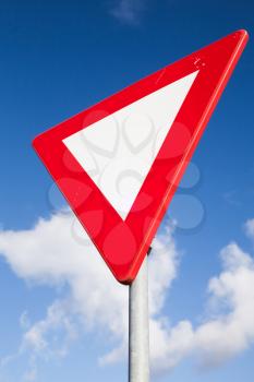 Give way road sign over blur cloudy sky, closeup vertical photo