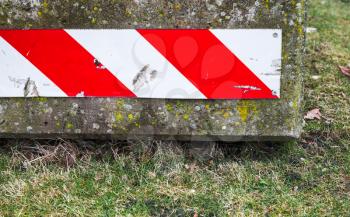 Concrete road block with red white striped warning sign lays on green grass