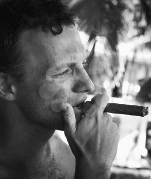 Young European man smokes big cigar, close up black and white face portrait with selective focus. Dominican Republic