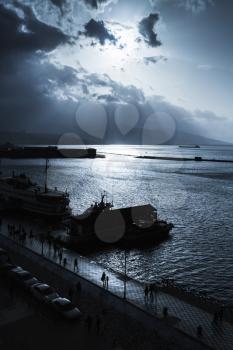 Dark dramatic sky with clouds and sunlight rays over sea. Port of Izmir. Blue toned photo filter effect