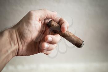 Dominican handmade cigar in male hand, closeup photo with selective focus over white wall background 