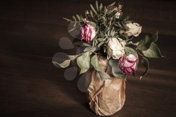 Bouquet of dried red and white roses stands on wooden table, closeup low key photo with soft selective focus