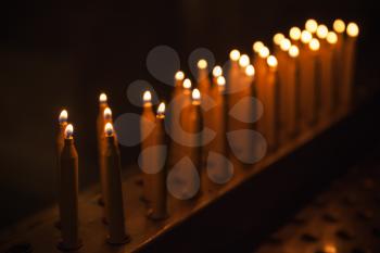 Burning prayer candles stand in a row, dark Catholic church interior