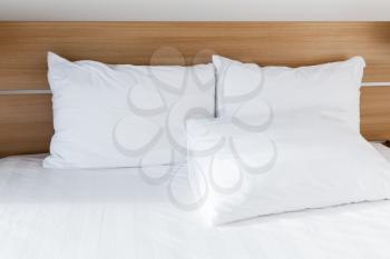 White pillows lay on wide empty bed with wooden headboard, bedroom interior fragment