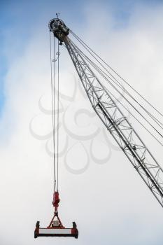 Steel crane boom with container spreader hanging on ropes