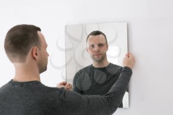 Studio portrait of young man standing near white wall with mirror