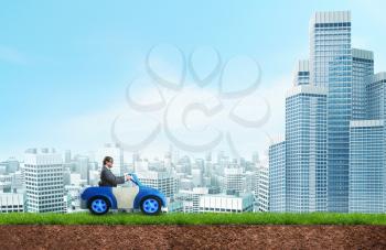 Young businessman driving a toy car towards the city