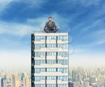 Businessman sits meditating on the top of a high building against city