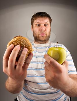 Portrait of man choosing between hamburger and green apple
