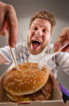 Portrait of happy man with knife and fork eating burger