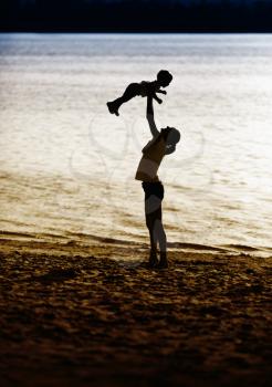 Mother holding her baby in silhouette at the beach. Toned