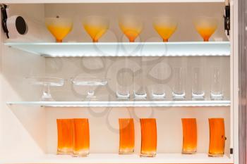 Modern kitchen cupboard full of various orange glasses