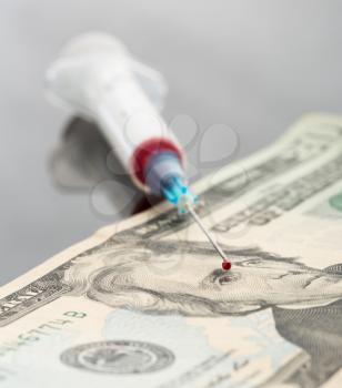 Syringe with blood drop on dollar note
